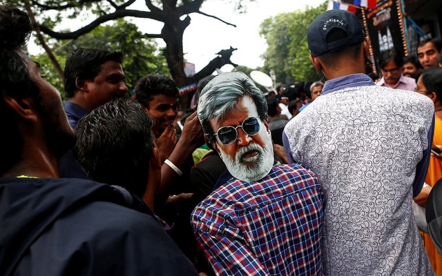 A fan wearing a mask of actor Rajinikanth waits outside a movie theatre on the eve of the release of Tamil film