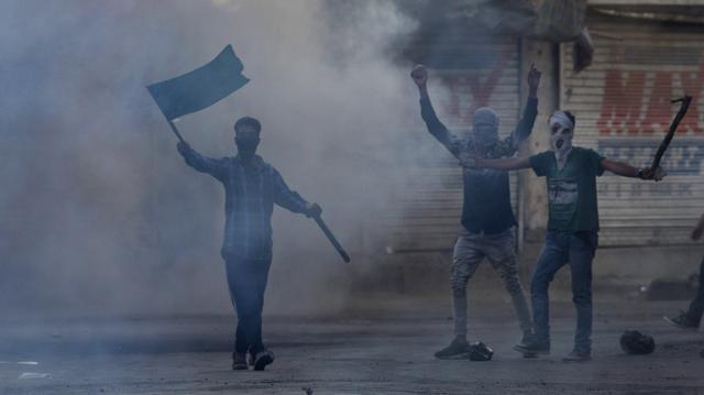 Masked Kashmiri protesters shout freedom slogans amid tear gas smoke during a protest in Srinagar