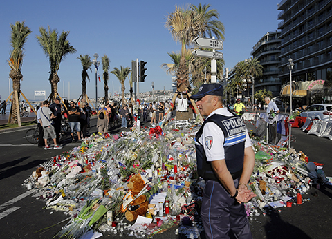 A police officer watches people gathering around a floral tribute for the victims killed during a deadly attack on the famed Boulevard des Anglais in Nice southern France Sunday