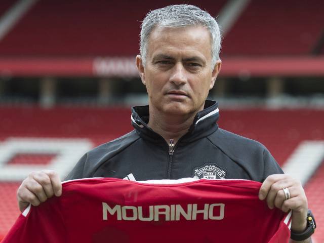 Manchester United's new Portuguese manager Jose Mourinho poses with a scarf on the pitch during