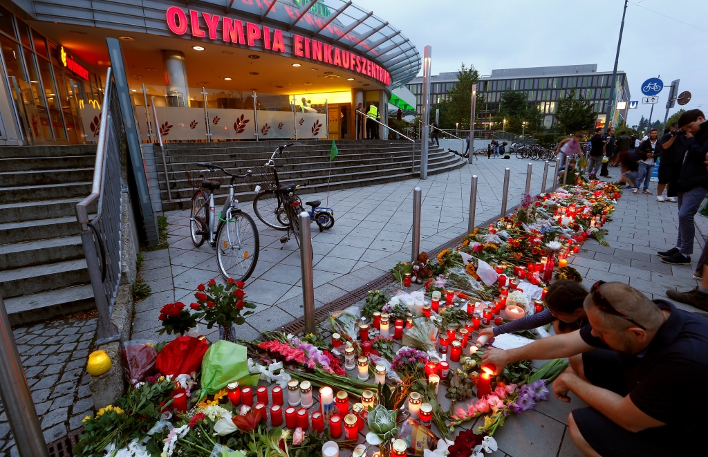 People light candles beside flowers laid in front of the Olympia shopping mall where yesterday's shooting rampage started in Munich