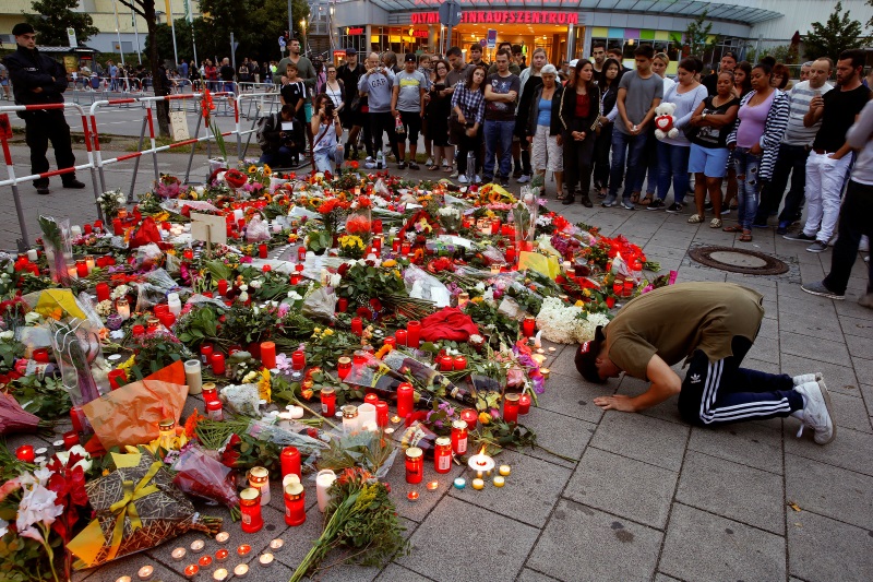 A man prays beside flowers laid at the Olympia shopping mall where shootings took place