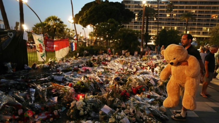 A man holds a giant teddy bear in front of a makeshift memorial near the Promenade des Anglais in Nice