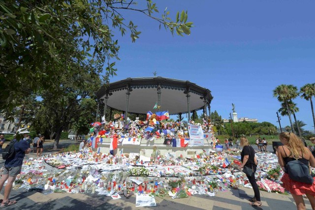 People stop near flowers left in tribute at a makeshift memorial to the victims of the Bastille Day truck attack along the Promenade des Anglais in Nice France