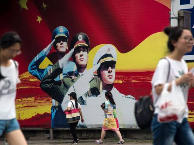 Pedestrians pass a military propaganda poster on a street in Shanghai