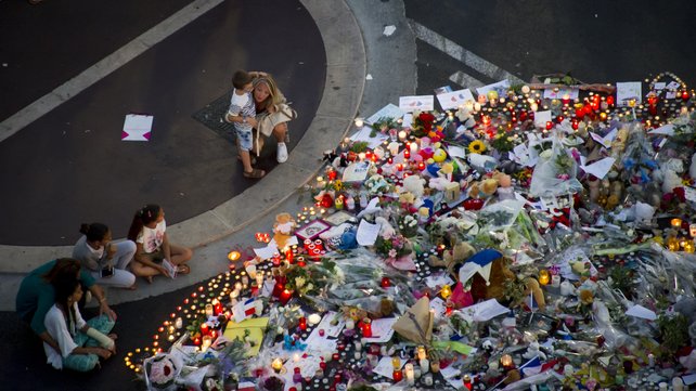 People gather at a makeshift memorial of flowers and candles on the 'Promenade des Anglais&#39