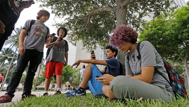 Pokemon Go players Ana Valentina Ojeda right and Jaeden Valdespino second from right check their smartphones as they look for Pokemon at Bayfront Park in downtown Miami as the