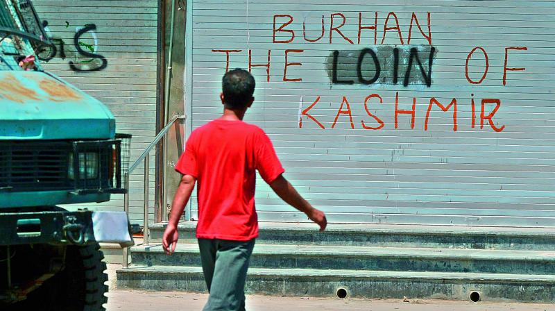 A civilian walks near a graffiti during a curfew in downtown Srinagar on Sunday. With one more civilian and a policeman dead the toll crosses 50