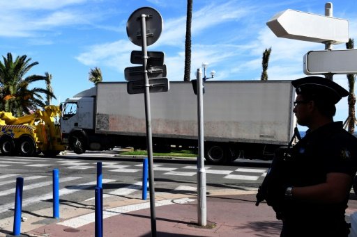 A police officer stands guard as the truck that was driven by a man through a crowd celebrating Bastille Day is towed away by a breakdown lorry