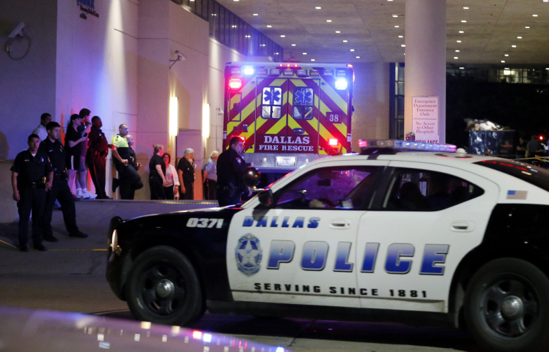 A Dallas police vehicle follows behind an ambulance carrying a patient to the emergency department at Baylor University Medical Center as police and others stand near the emergency entrance early Friday