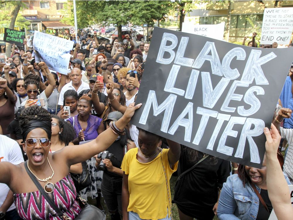 Daniella Felix bottom left raises her clenched fist as demonstrators gather in a tight circle during a Black Lives Matter rally in Nelson Mandela Park in Montreal Wednesday