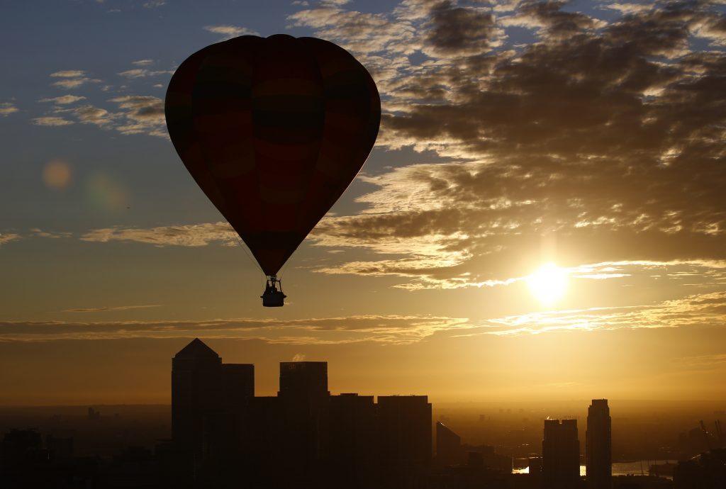 A hot air balloon rises into the early morning sky in front of the Canary Wharf financial district of London