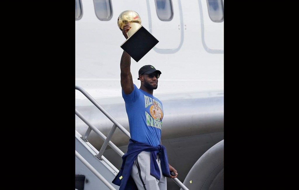 Cleveland Cavaliers&#039 Le Bron James raises the NBA Championship trophy after arriving at the airport Monday