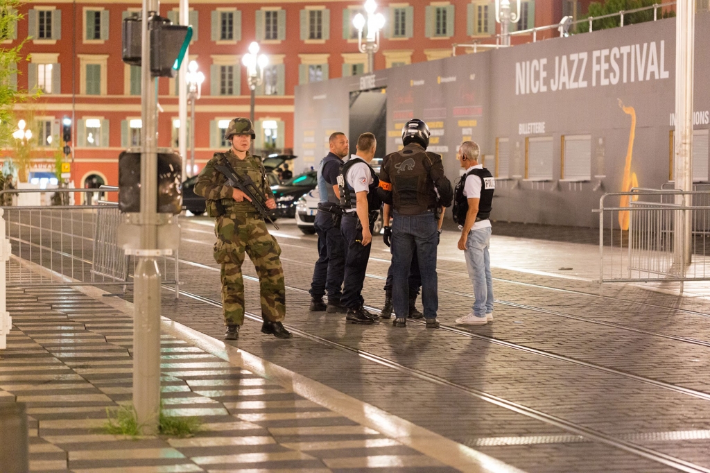 Police officers and a soldier stand by the sealed off area of an attack after a truck drove on to the sidewalk and plowed through a crowd of revelers who'd gathered to watch the fireworks in the French resort city of Nice southern France Friday July 15