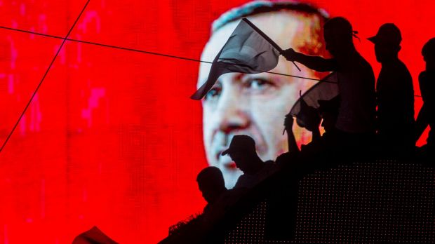 People wave Turkish flags in front of an electronic billboard displaying the face of President Recep Tayyip Erdogan at