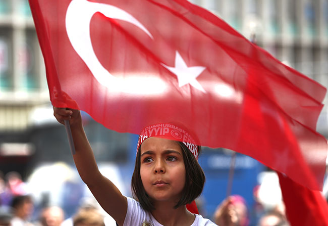 TURKEY. A Turkish girl wearing a headband bearing the name of Turkish President Recep Tayyip Erdogan waves her nation flags during a pro-government demonstration in front of the old parliament building in Ankara Turkey Wednesday