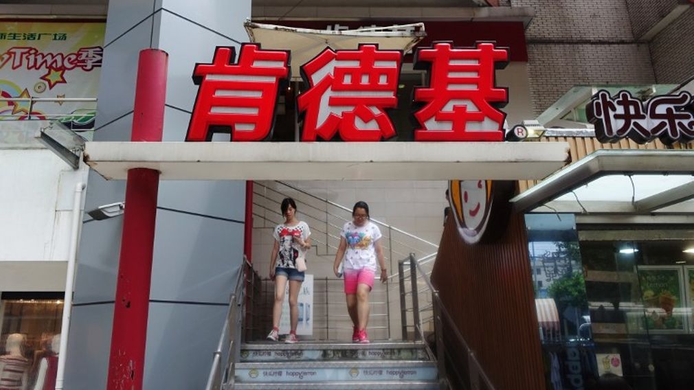 Two young women walk past signage for a KFC fast food restaurant in Shanghai