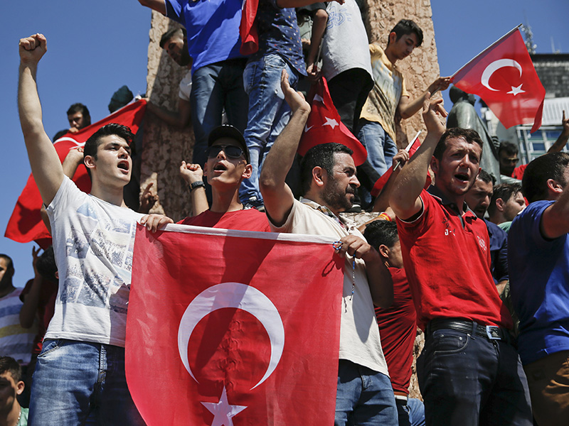 People wave Turkish flags as they stand around the Republic Monument in Taksim Square in Istanbul