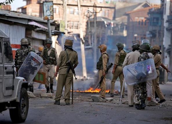 Policemen stand next to a burning handcart set on fire by demonstrators during a protest in Srinagar against the recent killings in Kashmir