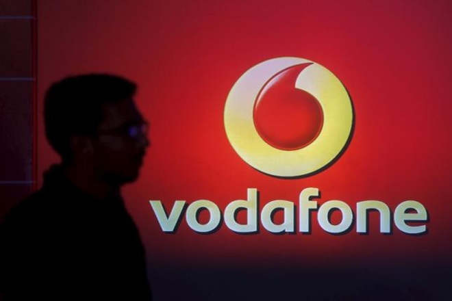 A man casts a silhouette onto an electronic screen displaying a Vodafone logo in Mumbai India in this file