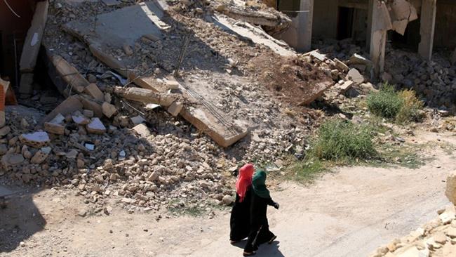 Women walk past damaged buildings along a street in the militant-held town of Da'il in Dara'a Governorate Syria