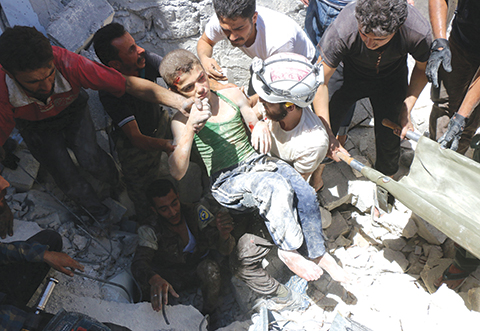 TOPSHOT- Syrian civil defence volunteers known as the White Helmets carry a young boy after they dug him out from under the rubble of buildings destroyed following reported air strikes on the rebel-held neighbourhood of Al Mashhad in the northern city