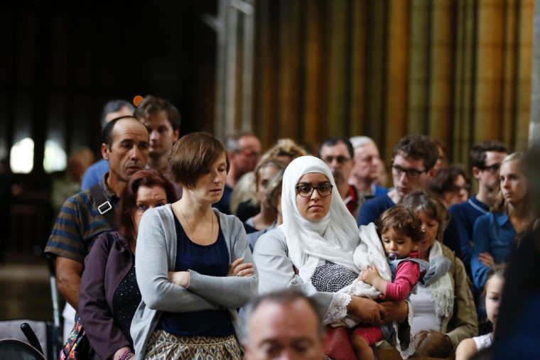 A Christian woman and a Muslim woman with her child stand side by side in Rouen Cathedral