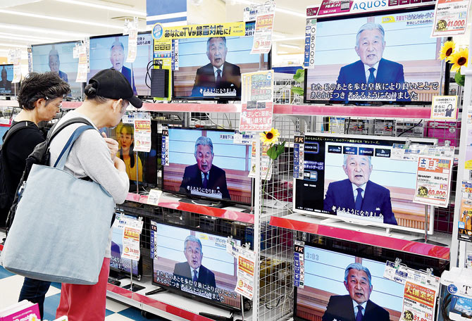 A couple looks at television screens showing a speech to the nation by Japanese Emperor Akihito. Pic  AFP