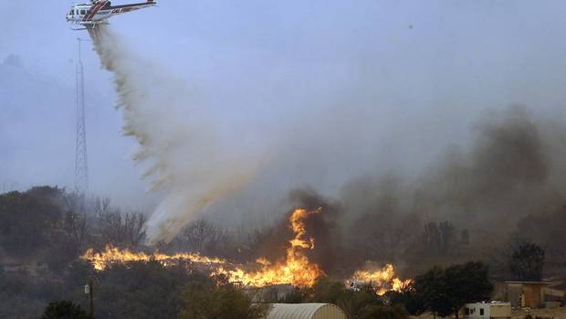 A helicopter drops retardant and water over flames in West Cajon Valley California