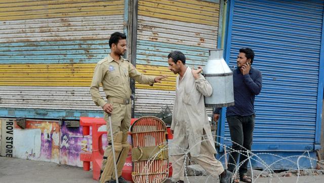 A policeman stops a milkman at a blocked road during the 45th day of curfew in Srinagar on Monday