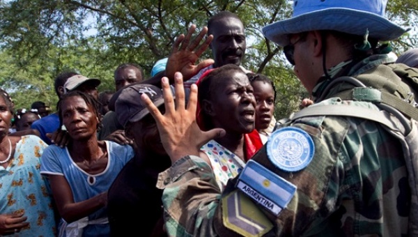 A soldier with the UN Stabilization Mission in Haiti gestures to local residents waiting to receive bottled water