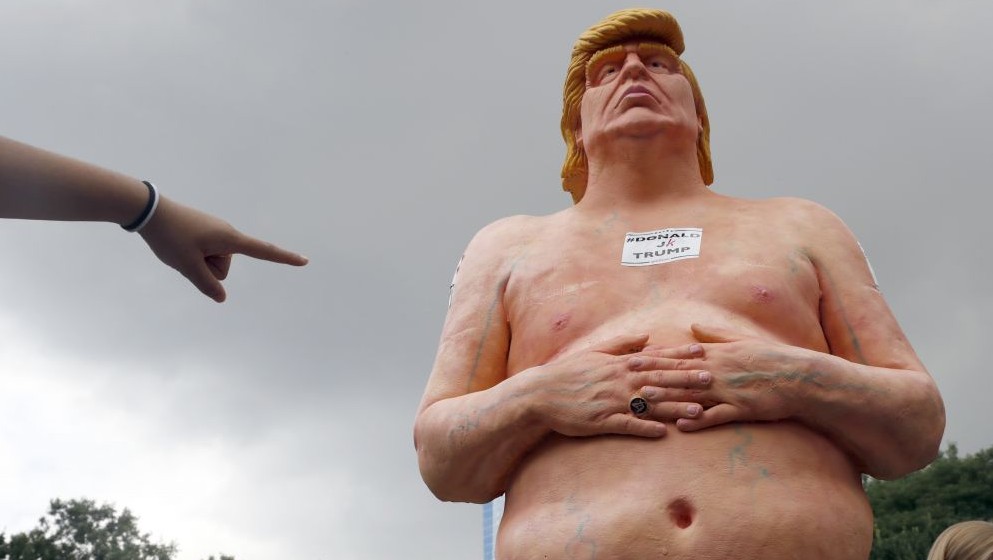 A woman points at a statue of a naked Republican presidential candidate Donald Trump