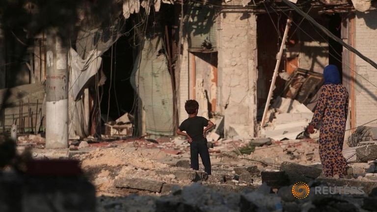 A woman walks with a boy on the rubble of damaged shops and buildings in Manbij Aleppo Governorate Syria