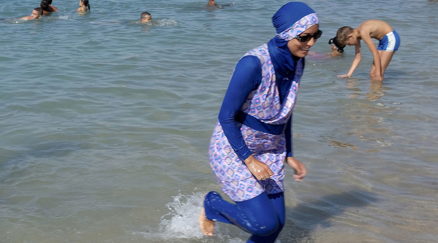 A woman wearing a burkini walks in the water on a beach in Marseille France