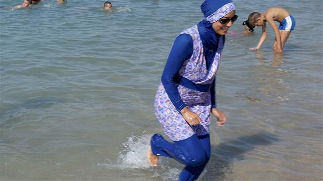 A woman wearing a burkini walks in the water on a beach in Marseille France