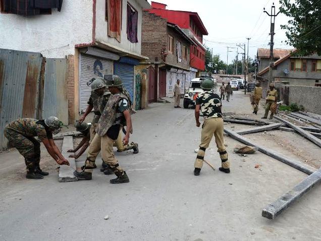 Policemen remove hurdles placed across a road by protesters in curfew-bound Srinagar on Thursday