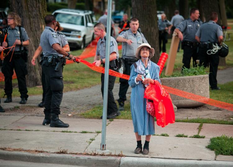 An elderly woman waits for the bus as members of the Milwaukee cops fence off Sherman Park