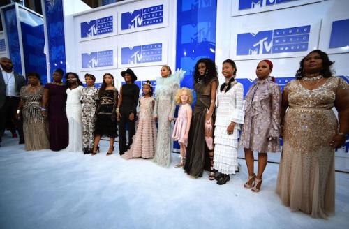 Women girls and man on white and blue walkway in dresses and outfits of various colors