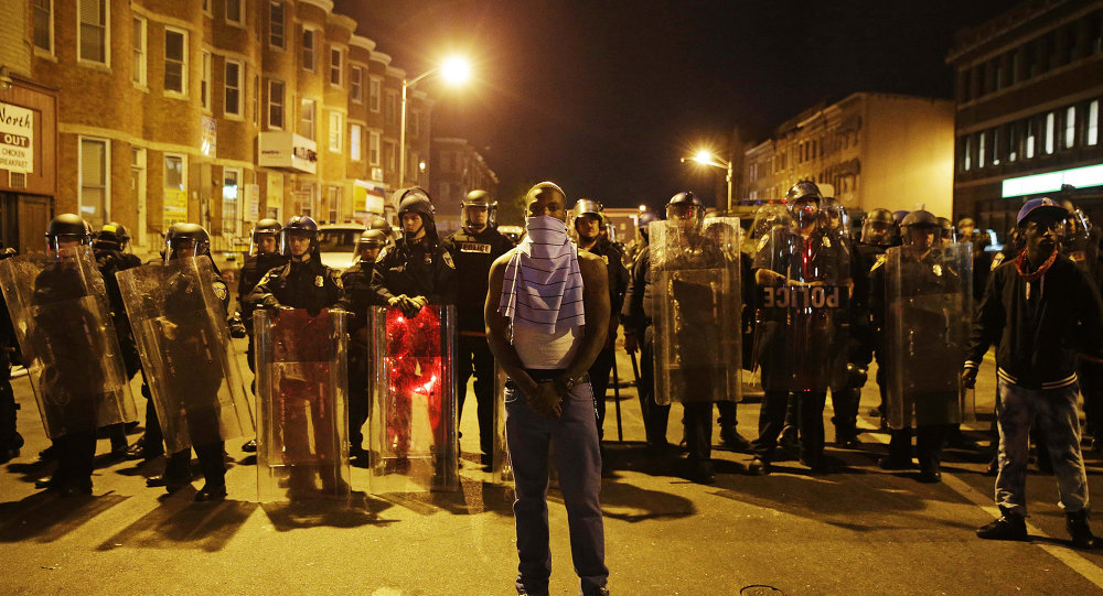 A man stands in front of a line of police officers in riot gear as part of a community effort to disperse the crowd ahead of a 10 p.m. curfew in the wake of Monday's riots following the funeral for Freddie Gray Tuesday