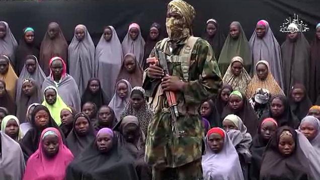 A screenshot from the video released purportedly by Boko Haram shows what it claimed is one of its fighters standing in front of some girls kidnapped from Chibok Nigeria in April 2014