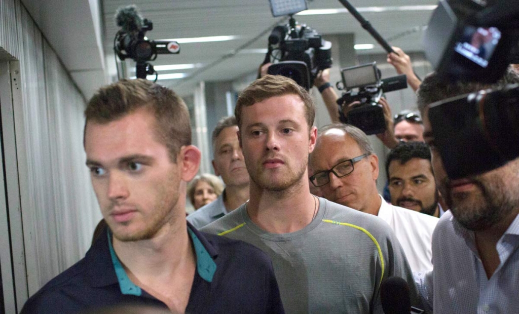 Journalists surround American Olympic swimmers Gunnar Bentz left and Jack Conger center as they leave the police station at Rio International airport early Thursday Aug. 18 2016