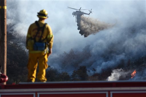 A San Bernardino County Fire Department firefighter watches a helitanker make a water drop on a wildfire seen from Cajon Boulevard in Devore Calif. Thursday Aug. 18 2016