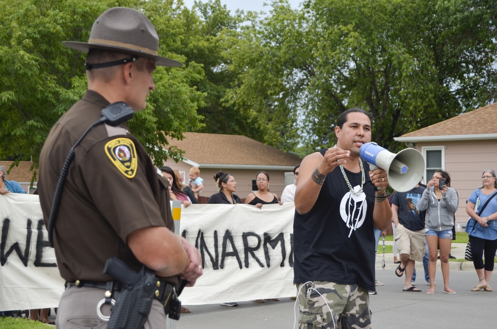 Dallas Goldtooth of the Indigenous Environmental Network voices his opposition to the Dakota Access Pipeline while law enforcement monitors the protest on the street in front of the North Dakota Capitol. Highway Patrol Capt. Bryan Niewind offered him a