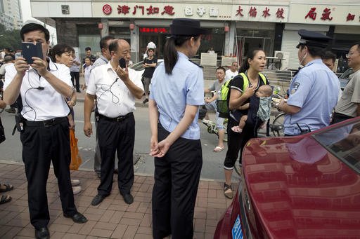 Yuan Shanshan third right the wife of detained Chinese lawyer Xie Yanyi carries her child as she talks to a police officer while other plain clothes security personnel film journalists near the Tianjin No. 2 Intermediate People's Court in northern Chin