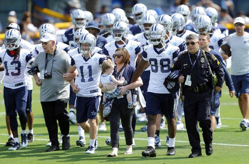 With her son Cameron in her arms Emily Crawford. center wife of slain DART officer Brent Thompson walks arm-in-arm with Dallas Cowboys wide receivers Dez Bryant and Cole Beasley as the team walked onto the field for the opening day of NFL foo