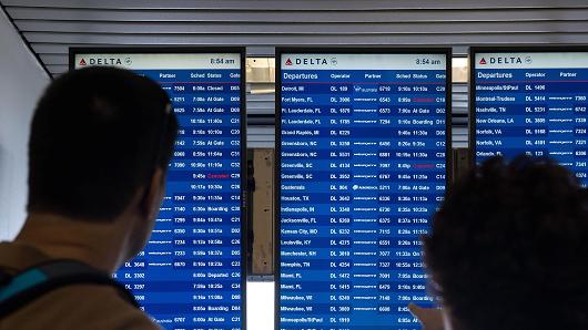 Travelers check the Delta departures board at La Guardia Airport