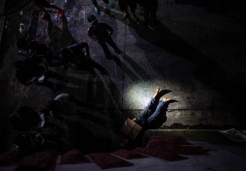 Police officers investigate the dead body of an alleged drug dealer his face covered with packing tape and a placard reading 'I'm a pusher,&#x27 in Manila