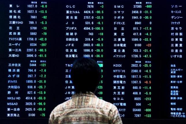 A woman stands in front of a display showing market indices at the Tokyo Stock Exchange in Tokyo