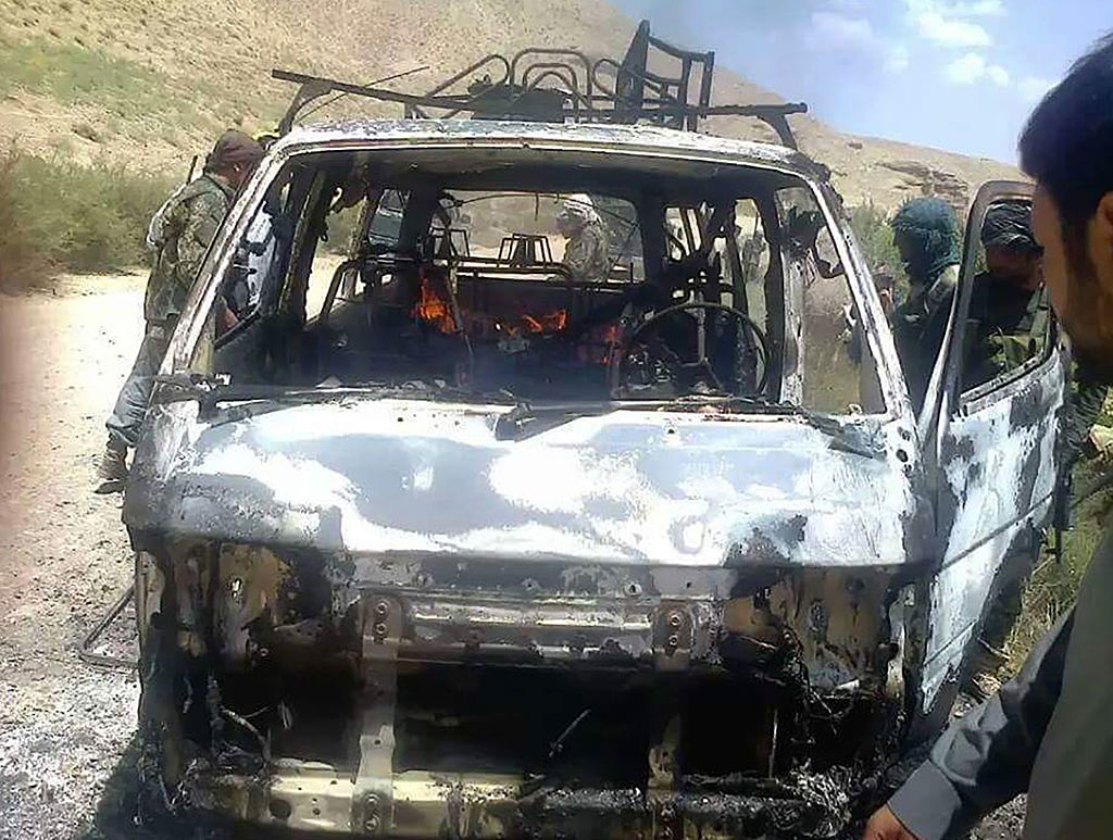 Afghan security forces inspect a burnt-out vehicle believed to have transported foreign tourists who came under attack from Taliban militants in western Herat province