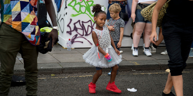 Notting Hill Carnival 2016 Children's Day. A little girl wearing a white party dress and red trainers dances in the street to a busking band